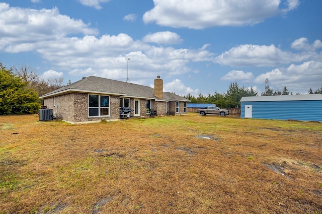 back of property with brick siding, central air condition unit, a lawn, and a chimney