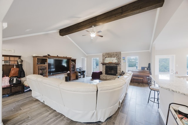 living room with lofted ceiling with beams, ornamental molding, a fireplace, wood finished floors, and a ceiling fan