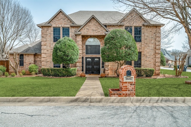 view of front facade with roof with shingles, brick siding, and a front lawn