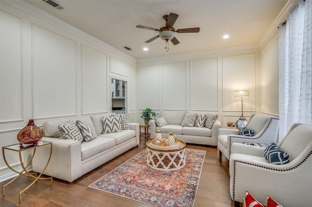 living room featuring ceiling fan, wood finished floors, visible vents, and a decorative wall