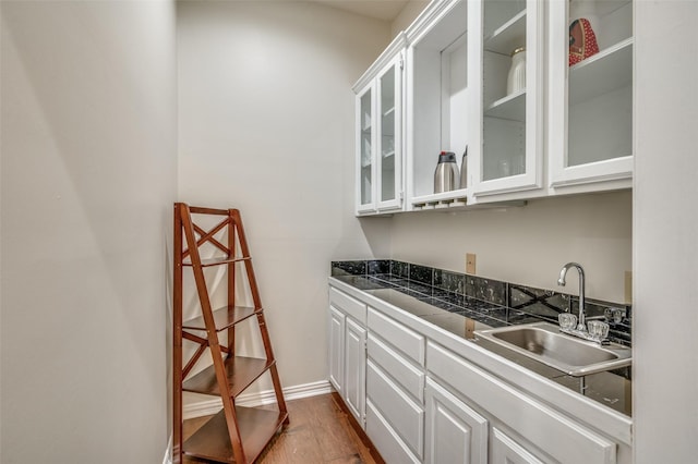 kitchen featuring dark wood-style flooring, a sink, white cabinets, dark countertops, and glass insert cabinets