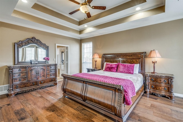 bedroom with a tray ceiling, multiple windows, hardwood / wood-style floors, and crown molding