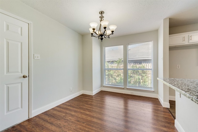 unfurnished dining area with a textured ceiling, baseboards, a chandelier, and dark wood-type flooring