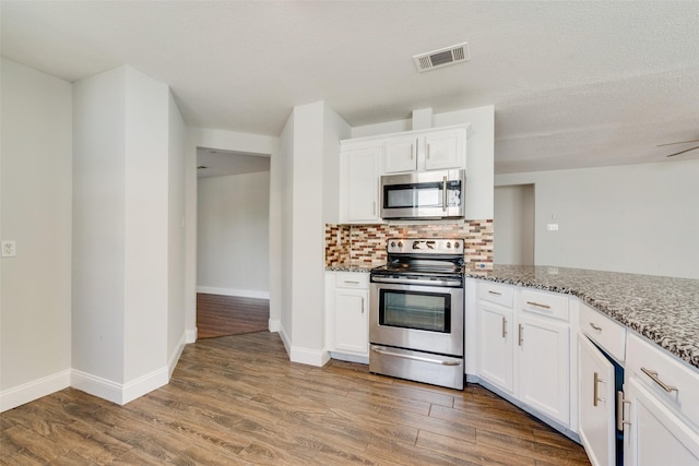 kitchen featuring light stone counters, visible vents, decorative backsplash, appliances with stainless steel finishes, and wood finished floors