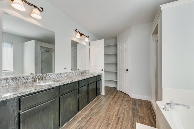 full bath featuring double vanity, wood finished floors, a sink, and a bath