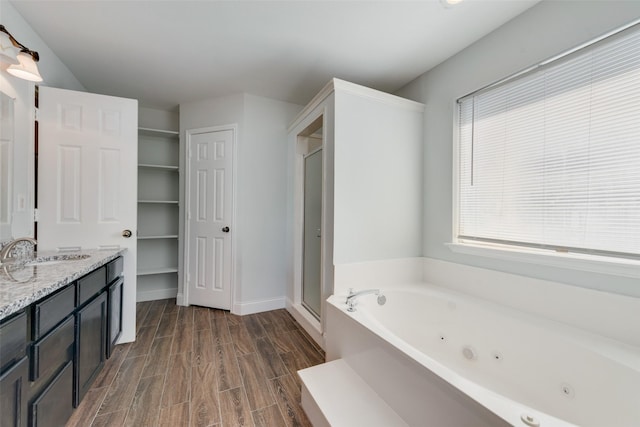 full bath with a stall shower, vanity, wood finished floors, a jetted tub, and baseboards