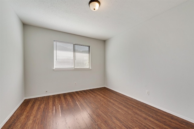 spare room featuring a textured ceiling, dark wood finished floors, and baseboards