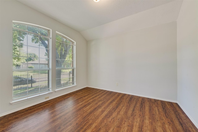 empty room featuring vaulted ceiling, dark wood-style flooring, plenty of natural light, and baseboards