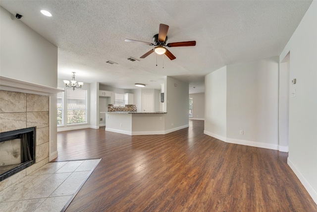 unfurnished living room with baseboards, visible vents, wood finished floors, a fireplace, and ceiling fan with notable chandelier