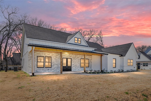 view of front facade with french doors, board and batten siding, roof with shingles, and a front lawn