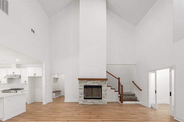 unfurnished living room featuring visible vents, a tile fireplace, stairway, and light wood-style floors