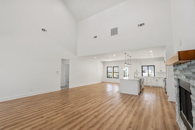 unfurnished living room with visible vents, a stone fireplace, and light wood-style floors