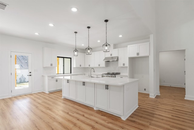 kitchen featuring under cabinet range hood, stove, white cabinets, and light countertops