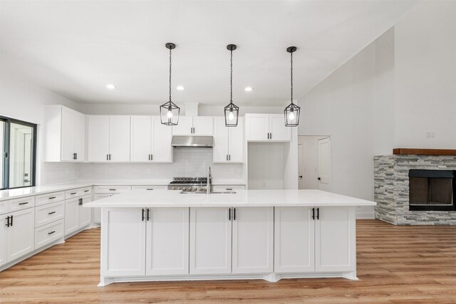 kitchen with under cabinet range hood, white cabinetry, light countertops, and a sink