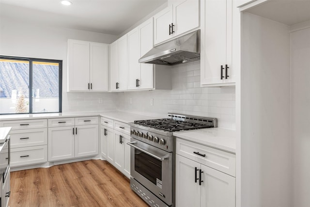 kitchen featuring high end stove, backsplash, under cabinet range hood, light countertops, and light wood-style flooring