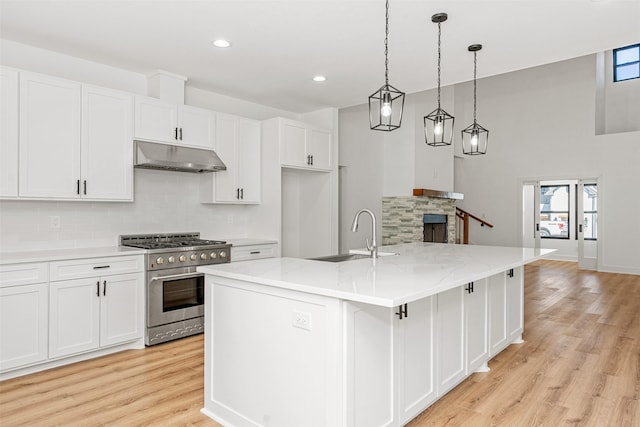 kitchen featuring under cabinet range hood, decorative backsplash, high end stainless steel range oven, white cabinetry, and a sink