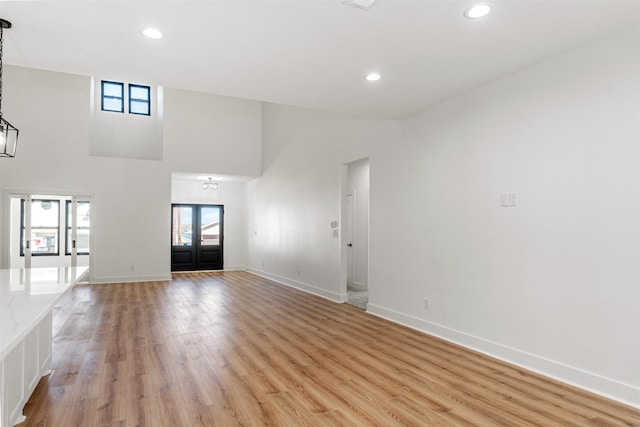 unfurnished living room with recessed lighting, light wood-type flooring, baseboards, and a high ceiling