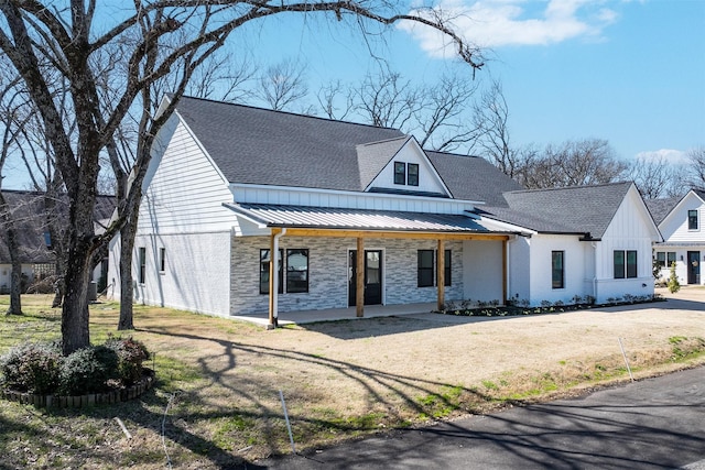 view of front of home with a front yard, a standing seam roof, covered porch, stone siding, and metal roof