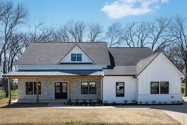 modern inspired farmhouse with stone siding, covered porch, and a front lawn