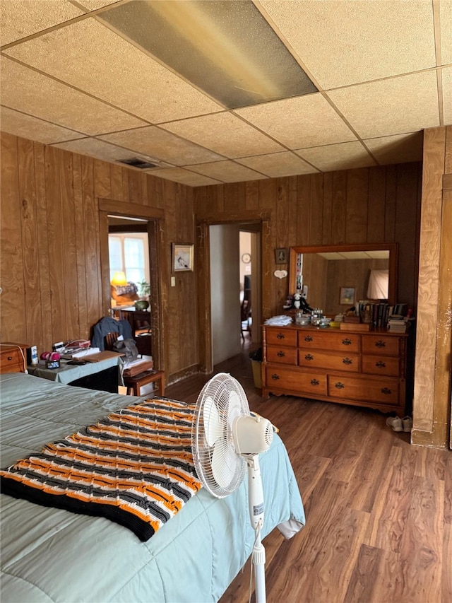 bedroom featuring a drop ceiling, wood finished floors, visible vents, and wooden walls