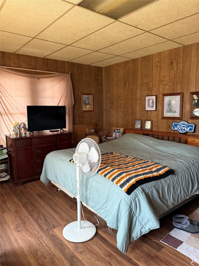 bedroom featuring a paneled ceiling, wood walls, and wood finished floors