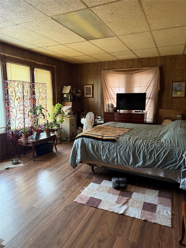 bedroom with a paneled ceiling, wood walls, and wood finished floors