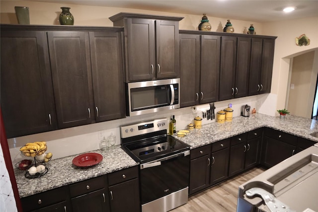 kitchen featuring electric range oven, light stone counters, stainless steel microwave, and light wood-style floors