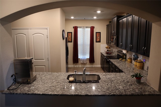 kitchen with arched walkways, stone counters, recessed lighting, stainless steel appliances, and a sink