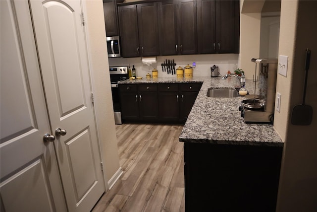 kitchen with stainless steel appliances, a sink, light wood-style flooring, and light stone countertops