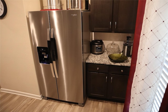 kitchen featuring dark brown cabinets, light stone counters, stainless steel refrigerator with ice dispenser, and light wood-style floors