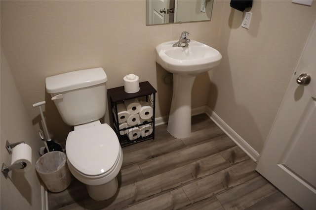 half bathroom featuring baseboards, a sink, toilet, and wood finished floors