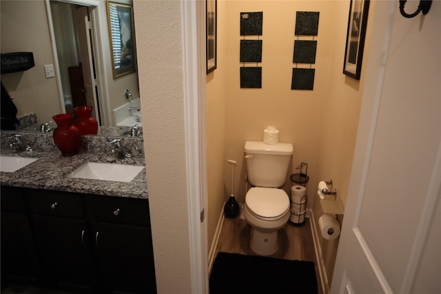 bathroom featuring double vanity, wood finished floors, a sink, and toilet