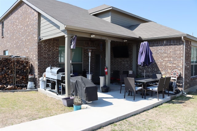 rear view of property with a shingled roof, a lawn, a patio, and brick siding