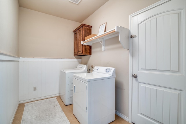 clothes washing area with light tile patterned floors, wainscoting, cabinet space, and separate washer and dryer