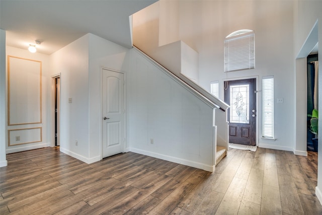 entrance foyer with stairway, wood finished floors, a towering ceiling, and baseboards