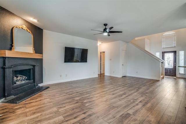 unfurnished living room with baseboards, a fireplace with raised hearth, ceiling fan, wood finished floors, and stairs