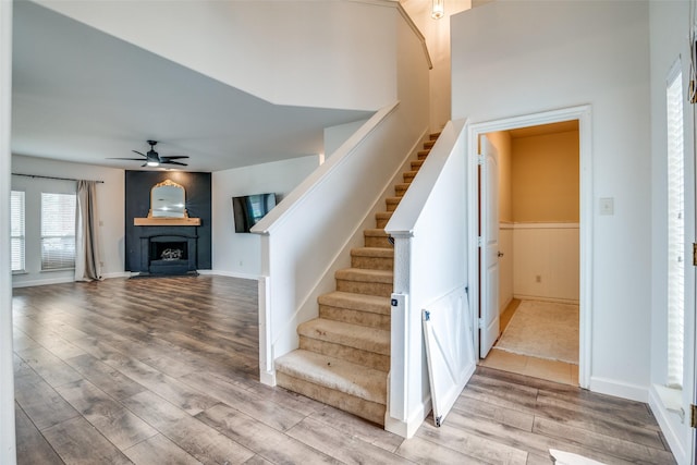 staircase featuring ceiling fan, a fireplace, baseboards, and wood finished floors