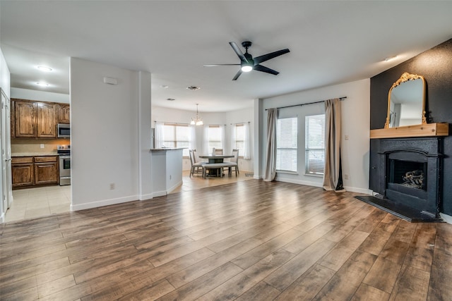 living area featuring visible vents, a fireplace with raised hearth, light wood-style flooring, baseboards, and ceiling fan with notable chandelier