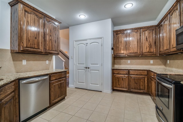 kitchen featuring light stone countertops, stainless steel appliances, backsplash, and light tile patterned flooring