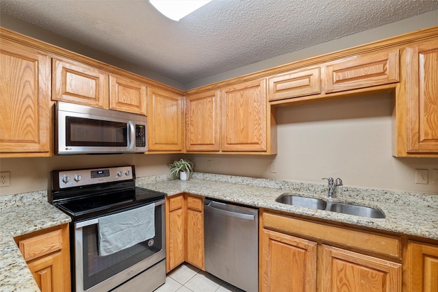 kitchen featuring a textured ceiling, light tile patterned flooring, a sink, appliances with stainless steel finishes, and light stone countertops