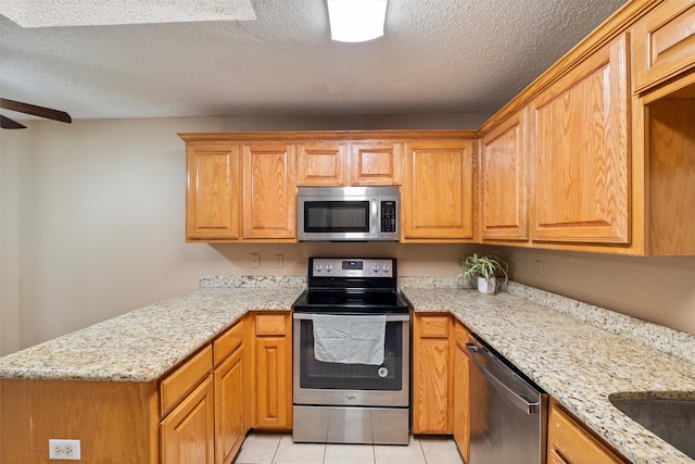 kitchen featuring appliances with stainless steel finishes, light stone counters, a peninsula, a textured ceiling, and light tile patterned flooring