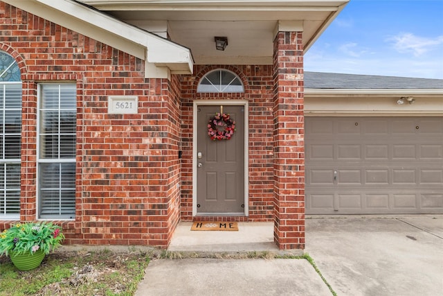 entrance to property featuring a garage, concrete driveway, brick siding, and a shingled roof