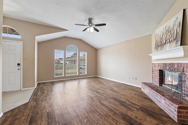 unfurnished living room with a brick fireplace, a ceiling fan, vaulted ceiling, and wood finished floors