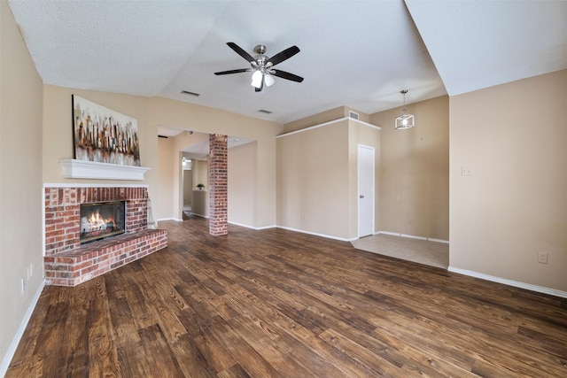 unfurnished living room featuring a brick fireplace, a ceiling fan, visible vents, and wood finished floors