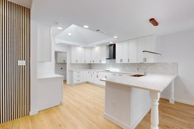 kitchen with black electric stovetop, a peninsula, a sink, visible vents, and wall chimney range hood