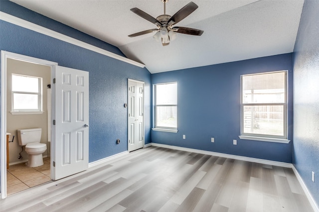 unfurnished bedroom with a textured wall, multiple windows, vaulted ceiling, and wood finished floors