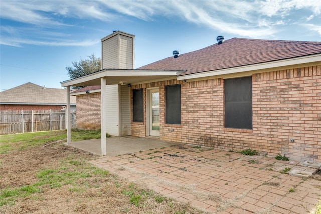 back of property with brick siding, a shingled roof, fence, and a patio