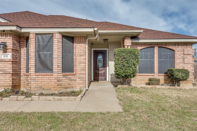 view of front of property featuring a shingled roof, a front yard, and brick siding