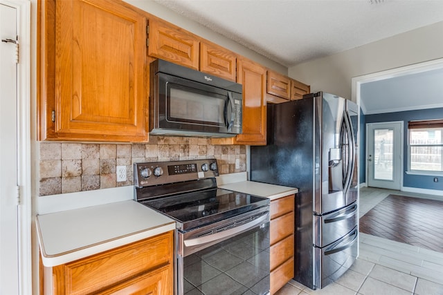 kitchen featuring stainless steel appliances, brown cabinets, light countertops, and decorative backsplash