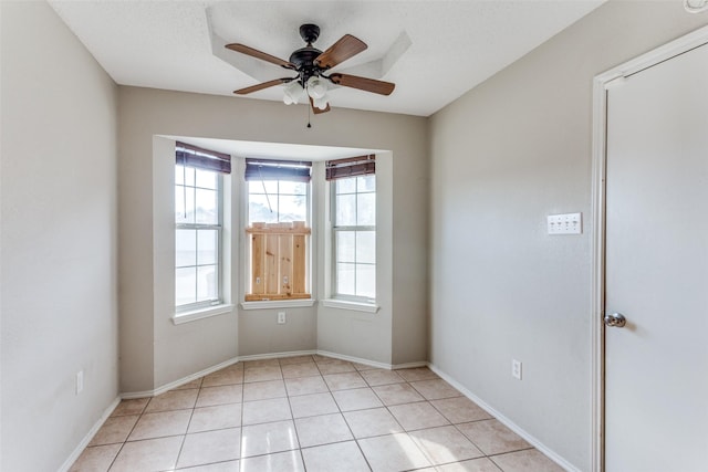 empty room featuring light tile patterned flooring, ceiling fan, a textured ceiling, and baseboards